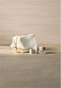 A luxurious white cosmetic pouch with a gold zipper next to 3 skincare samples on top of grey marble surface in neutral mood lighting